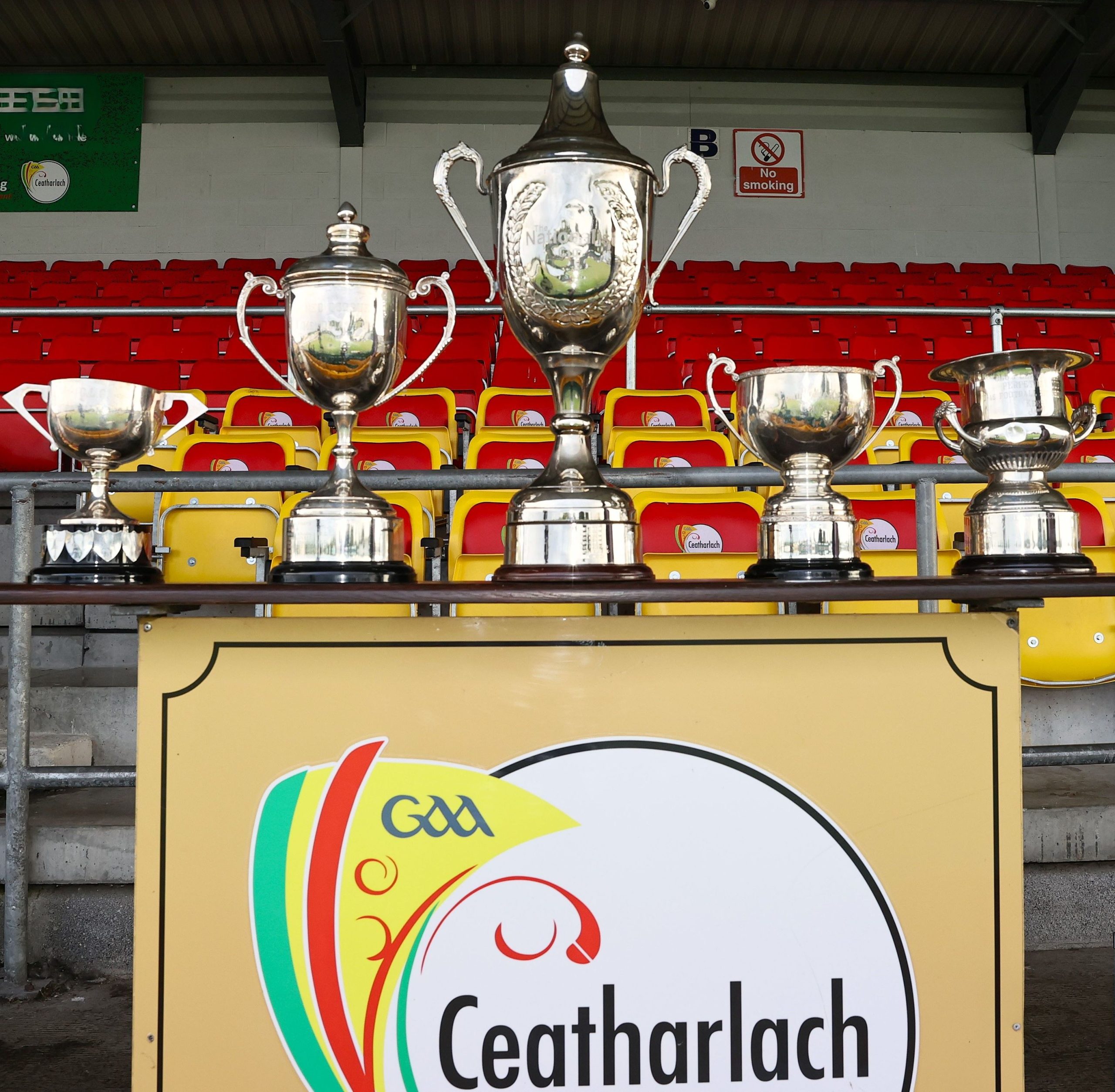 Cups Club Football launch 25 Aug 27th NCPJPG 1 1 Row of shiny trophy cups displayed on a yellow panel with red stadium seats in the background.